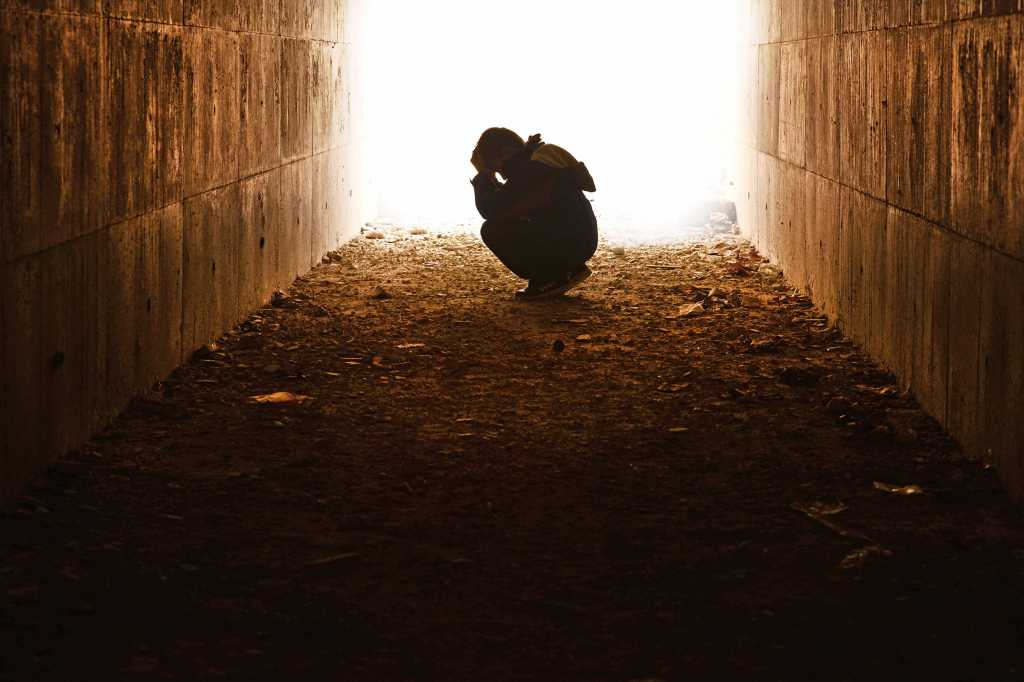Young person distressed, head in their hand waiting alone in tunnel.