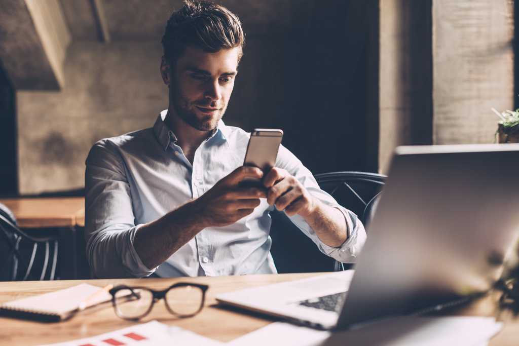 A young business man, text messaging at his desk.