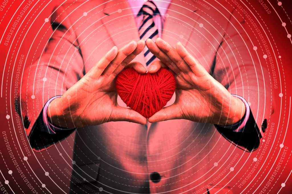 A businessman holds a red woolen heart surrounded by abstract binary circuits.