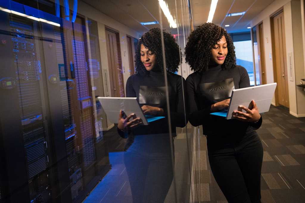 woman using a laptop stands outside a server room / data center / coder / developer / programmer