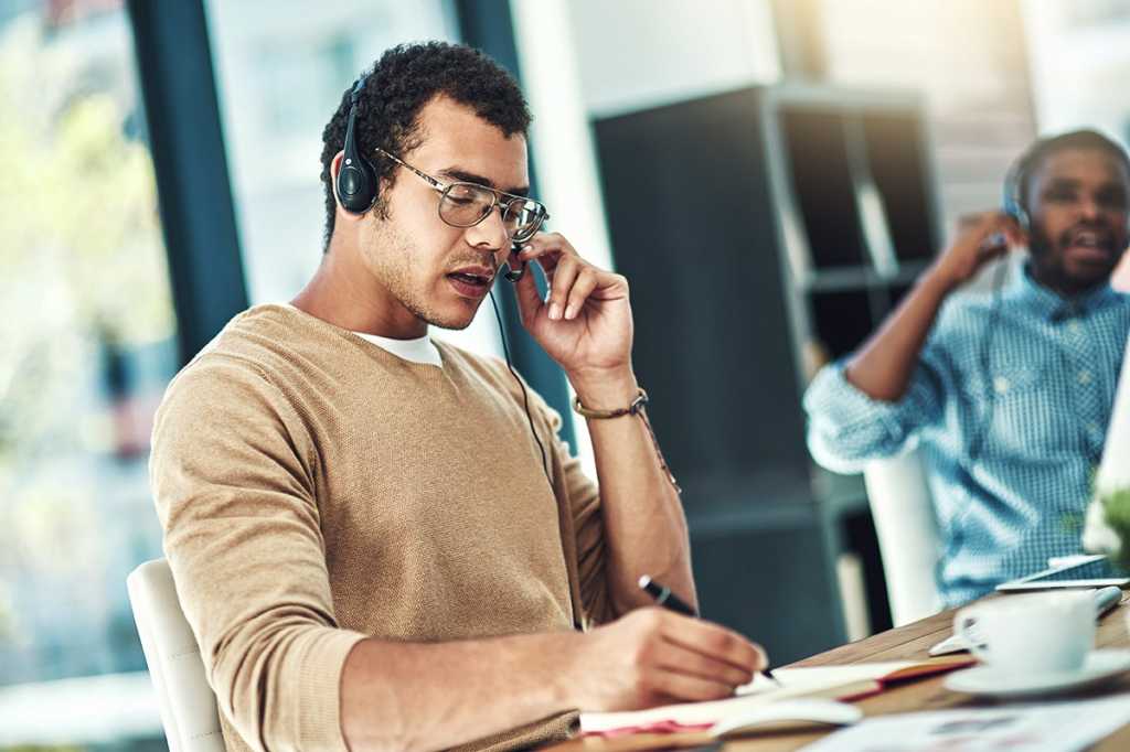 A man speaking into the microphone of a headset while sitting at a computer.