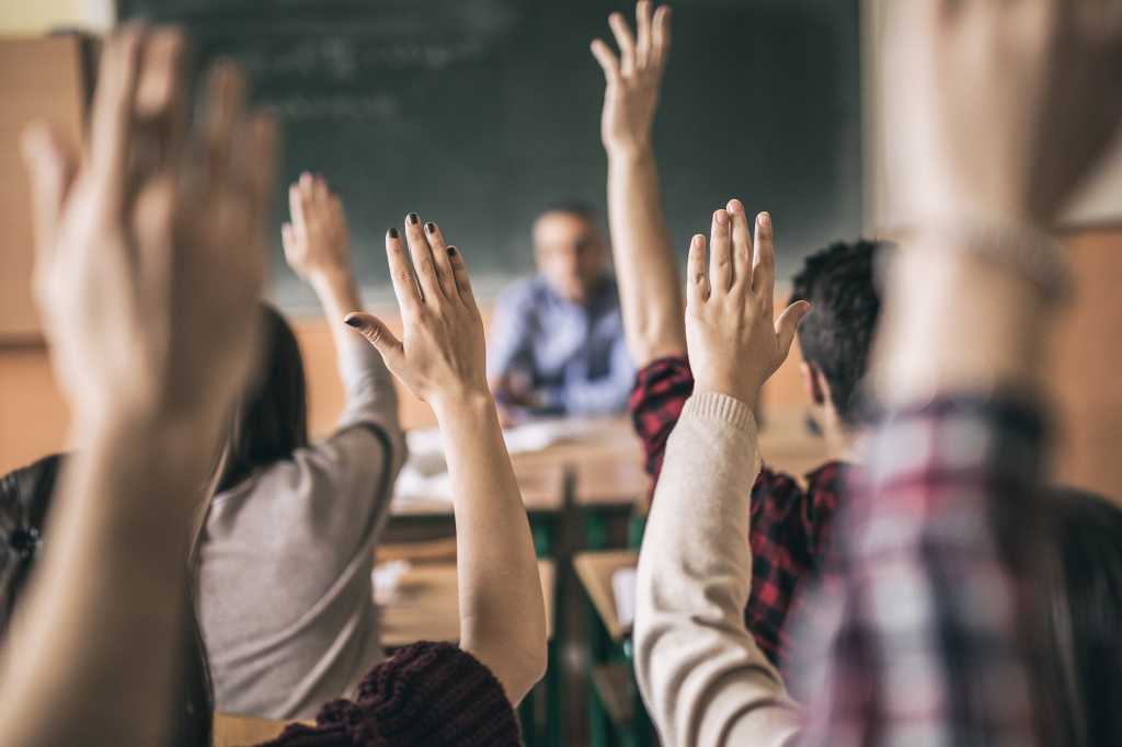 Rearview students with hands up teacher in background [students, education, question time]