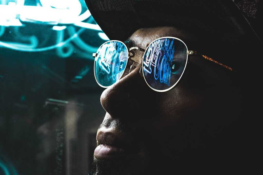 Abstract data/characters from neon lights are reflected in eyeglasses in this street portrait.