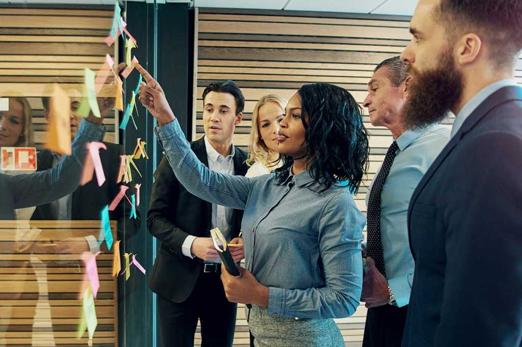 diverse group people collaborate using Post-It notes to strategize on a glass wall