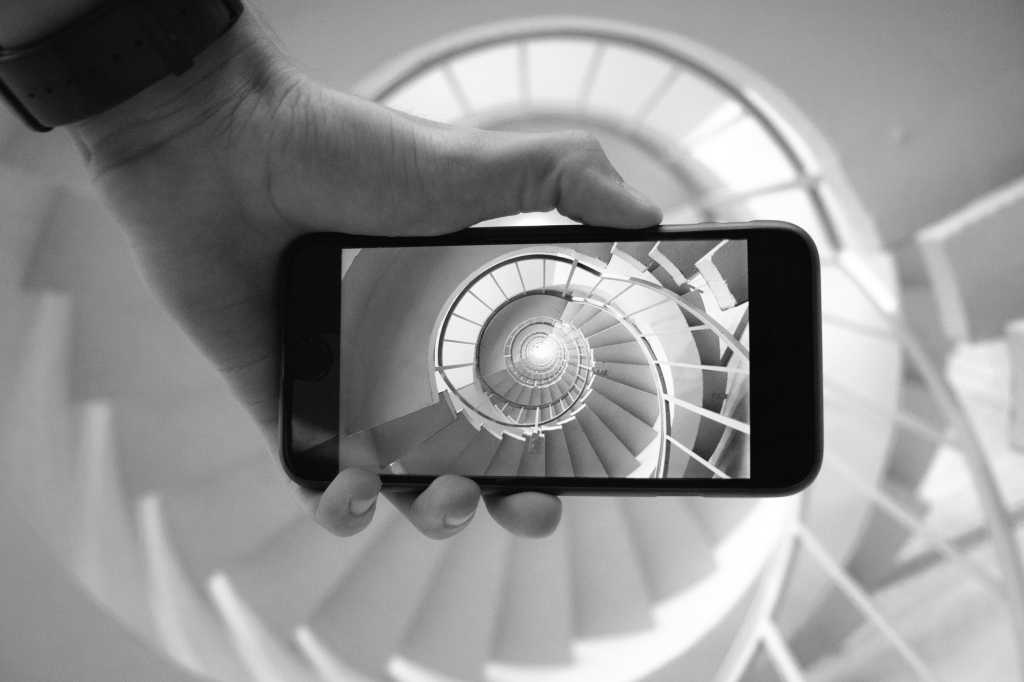hand holding smartphone with spiral staircase nautilus shell infinity by simon marsault via unsplash
