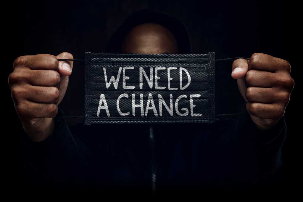 Hands hold a face mask saying, 'We need a change.'  [diversity / inclusion/ allyship / anti-racism]