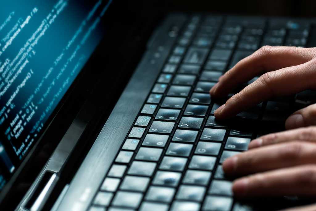 Hands type on a laptop keyboard in a dark workspace.