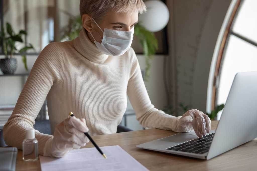 A laptop user wears a face mask and gloves in a post-COVID office workspace.