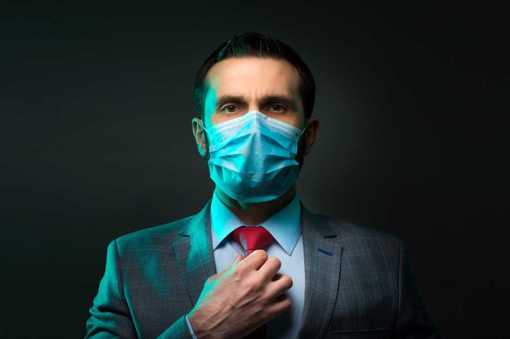 A man in suit wears a protective face mask. / Post-COVID office workspaces