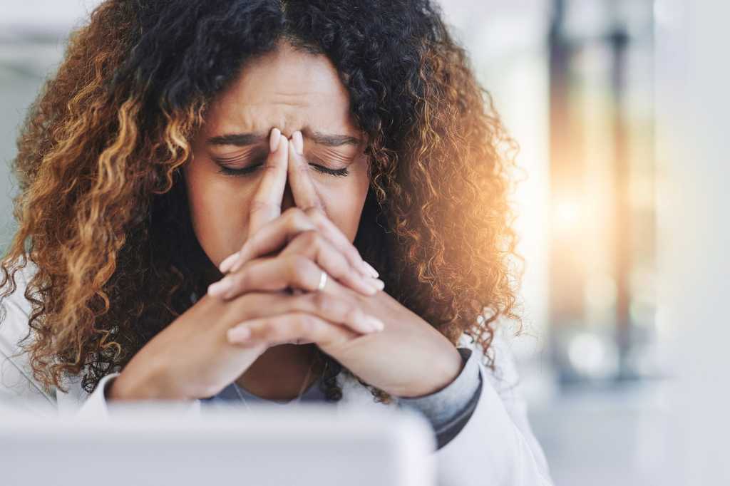 A miserable, stressed laptop user holds her head in her hands.