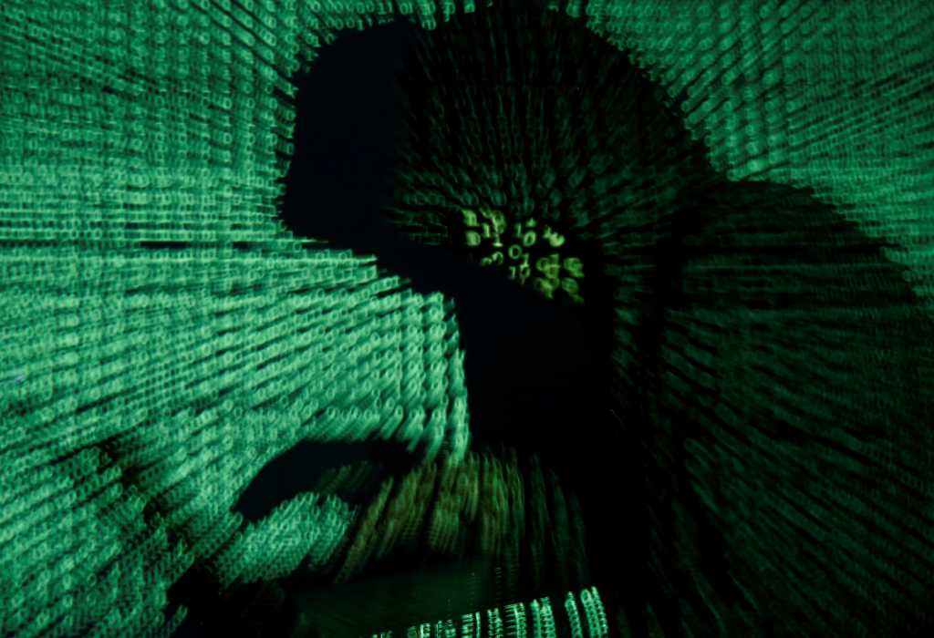 Hooded man hacking computer with green binary background