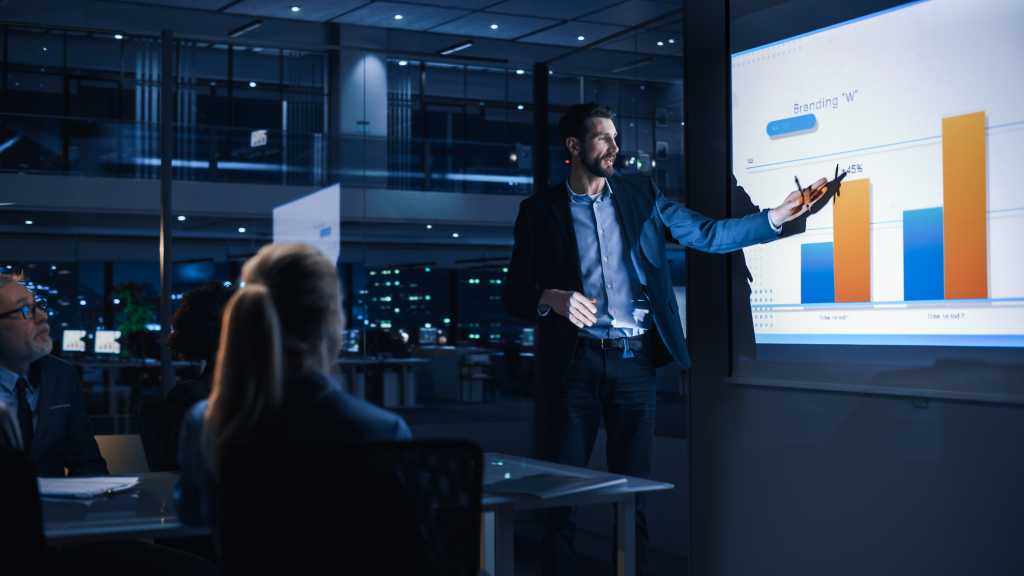 Conference Business Meeting Presentation: CEO Businessman Shows Data to Group of Investors, Businessspeople. Projector Screen Shows Graphs, Product Sales, Revenue Growth Strategy, e-Commerce Analysis