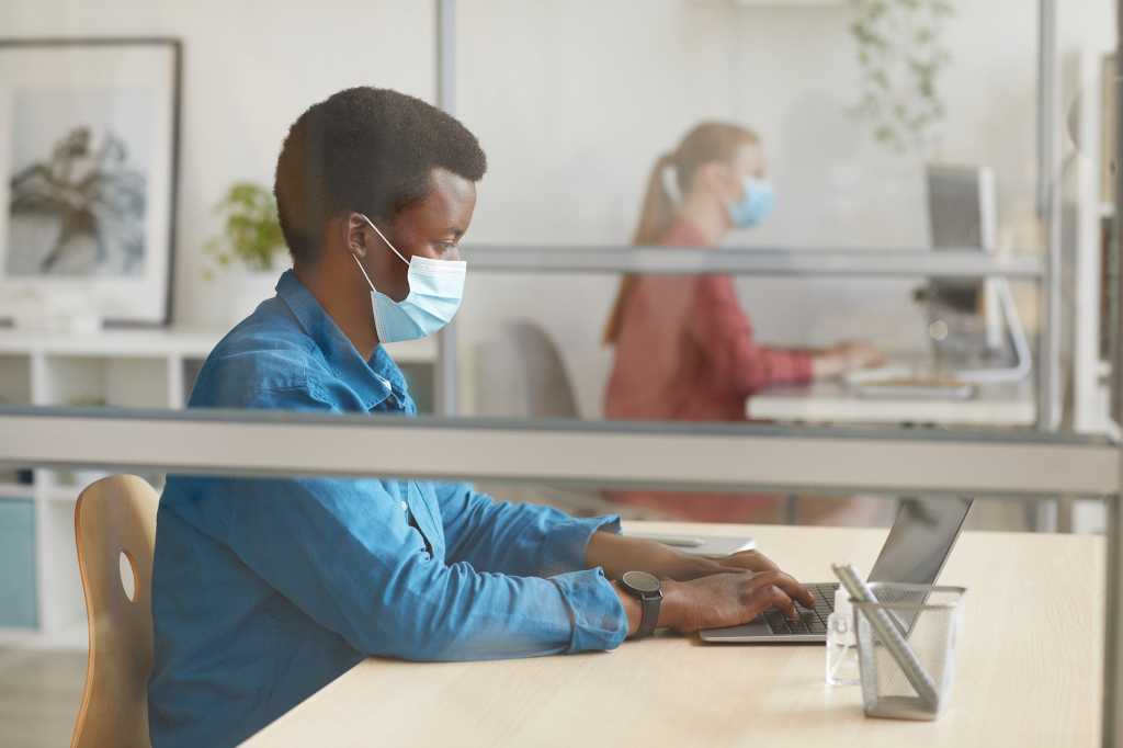 Staff wearing masks work at partitioned desks in an office workspace.