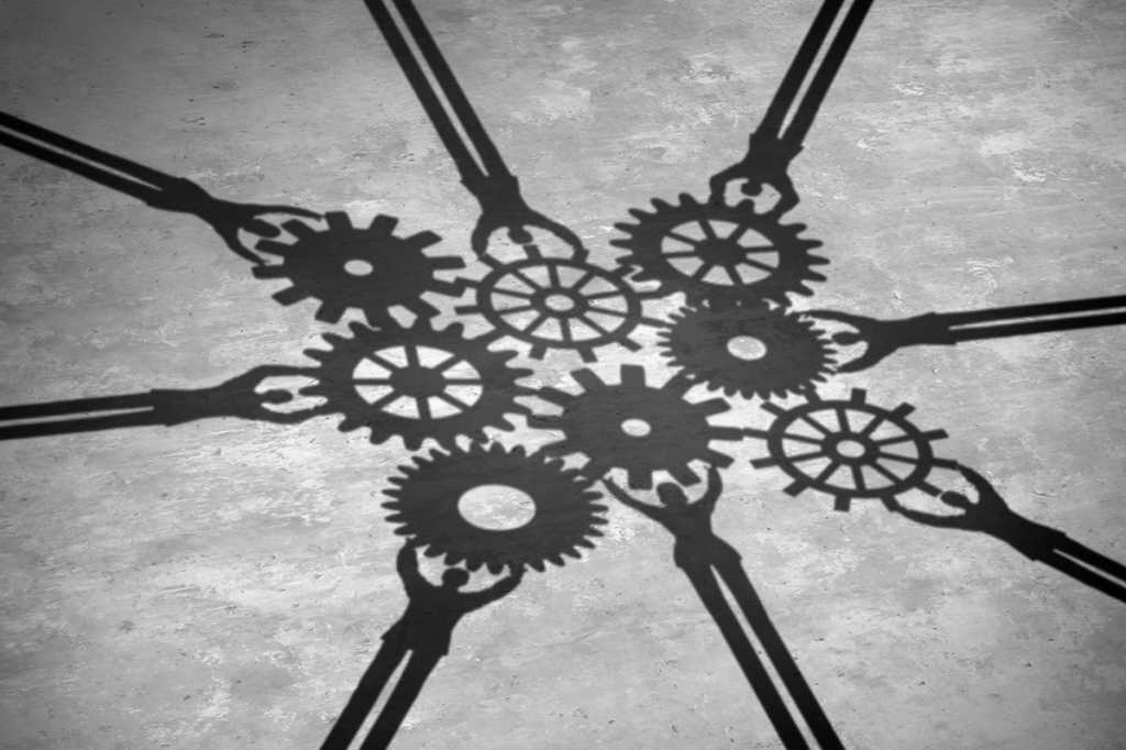 shadows of team figures collaborating, each holding up gears that work together