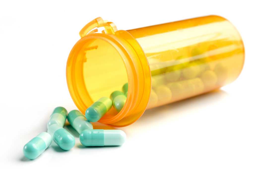 Orange prescription bottle with green pills spilling out