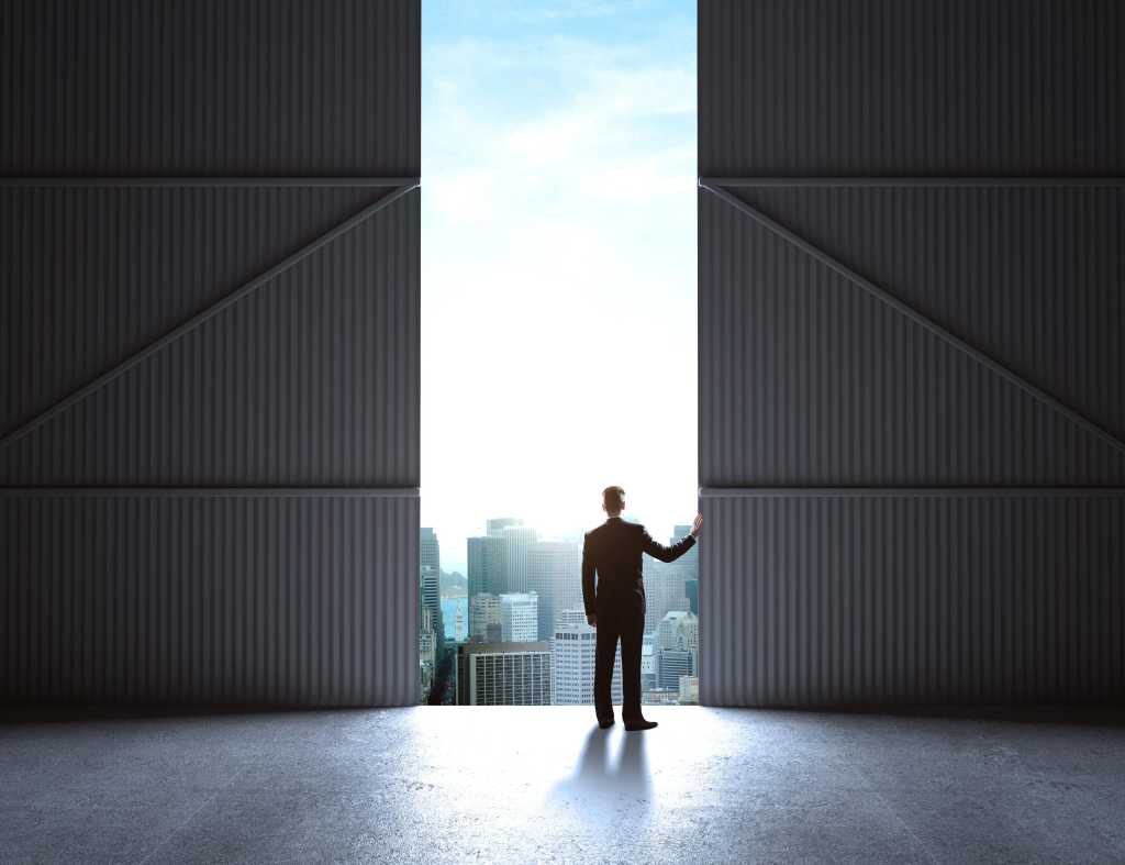 Man in hanger looking out over city with sun shining in