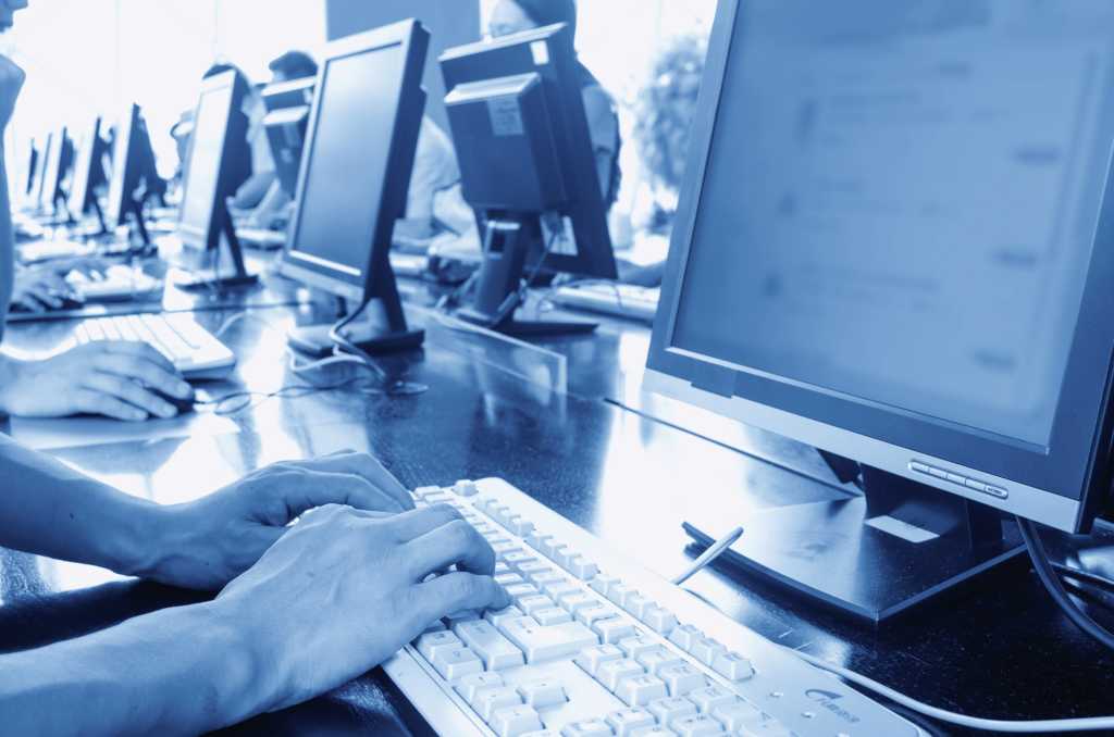 blue sepia photo of people seated at row of computers in a computer lab or classroom