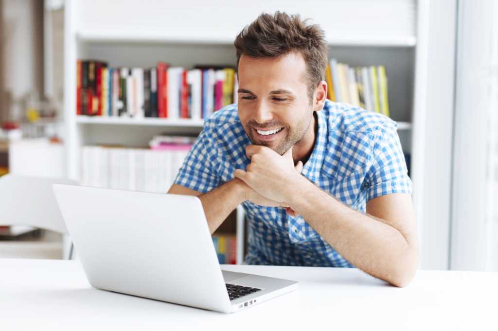 millennial smiling seated at desk looking at laptop