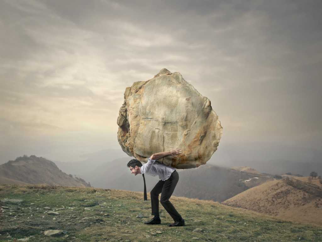 young executive walking up a hill with boulder on back