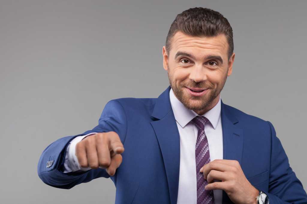 Dapper man in blue suit pointing at camera confidently