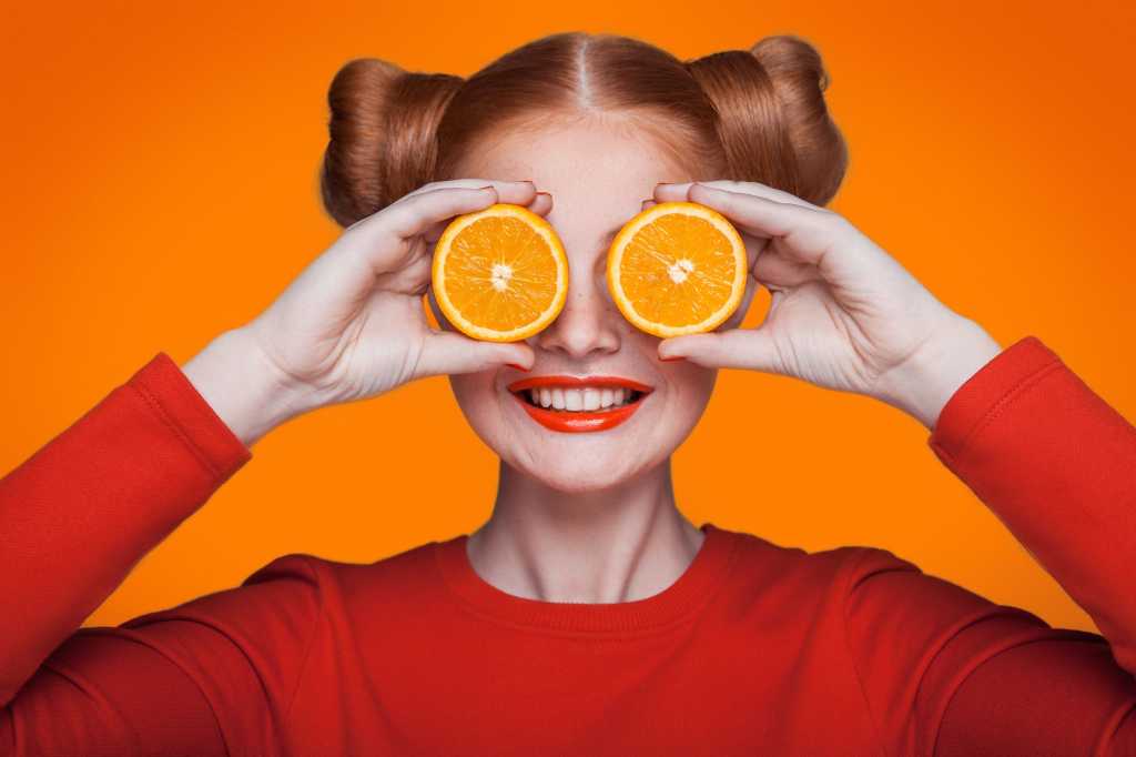 Fun girl with red lipstick holding orange slices over her eyes