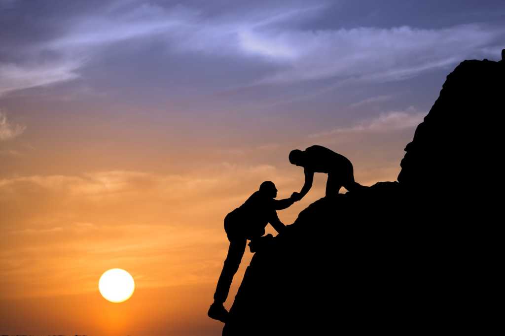 Man helping man up mountain showing teamwork support mentor