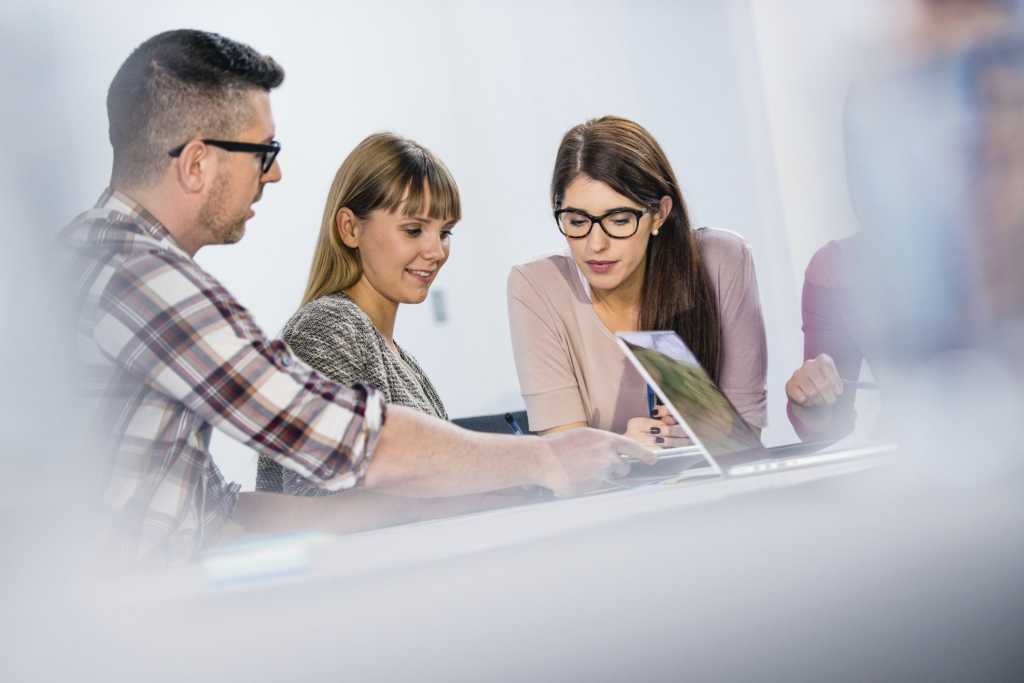 Young group of employees collaborating at desk with laptops