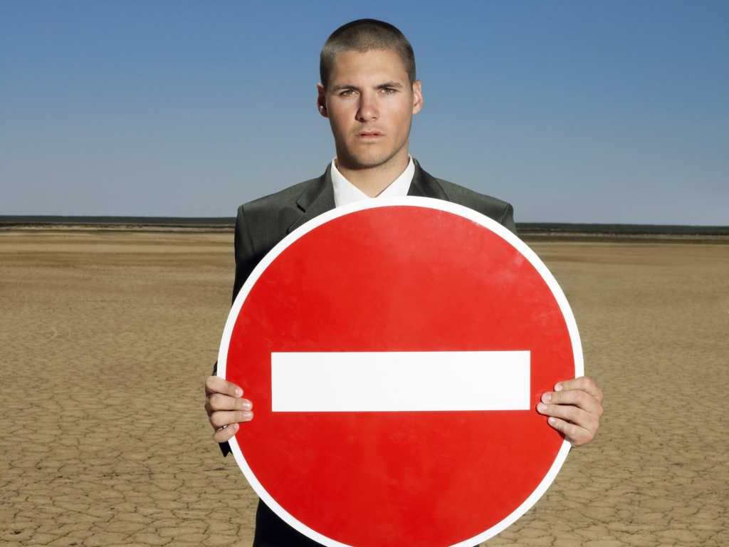 young man in suit on the beach holding red do not enter sign