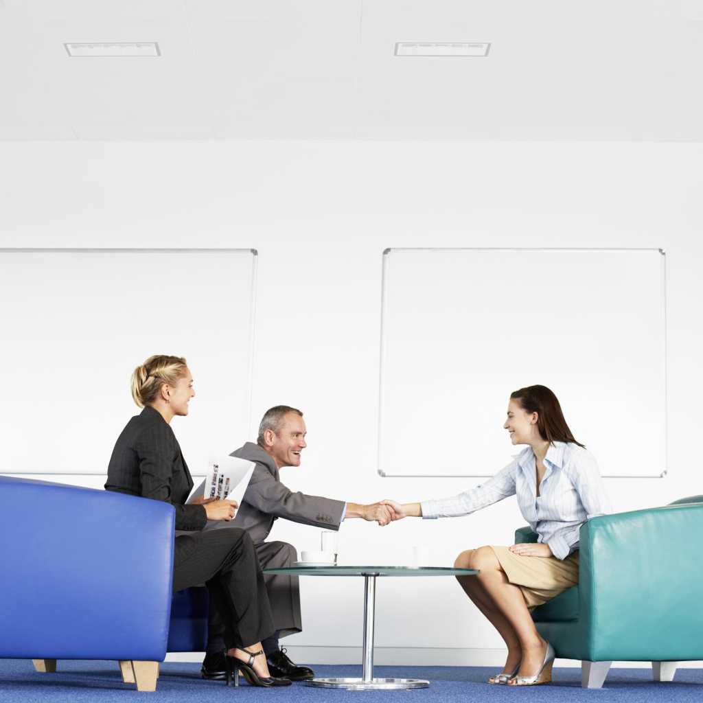 3 male and female executives sitting in office shaking hands and interviewing
