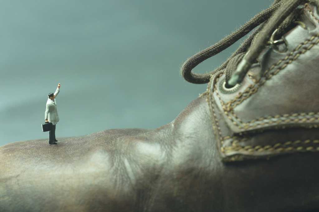 miniature man standing on oversized shoe like an underdog