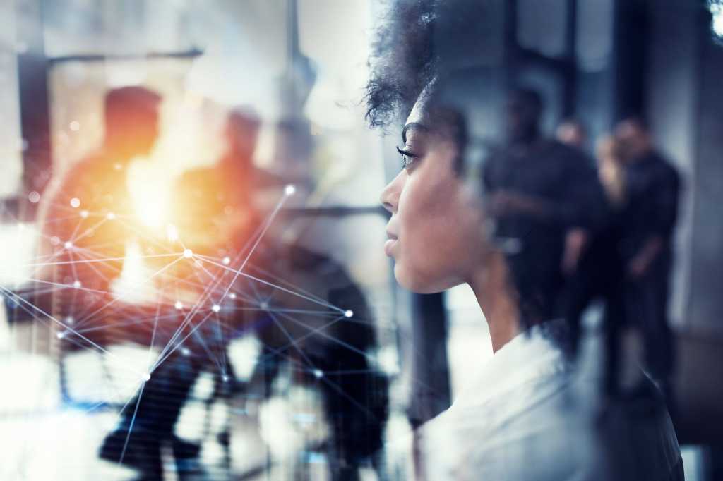 A businesswoman looks into the distance amid abstract technology, colleagues in background.