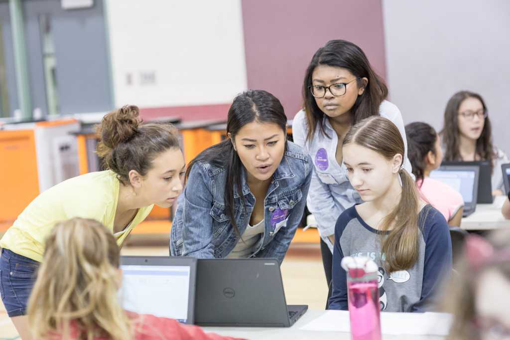 Hackergal hackathon: Young girl at laptop participating in coding hackathon with mentors and teachers
