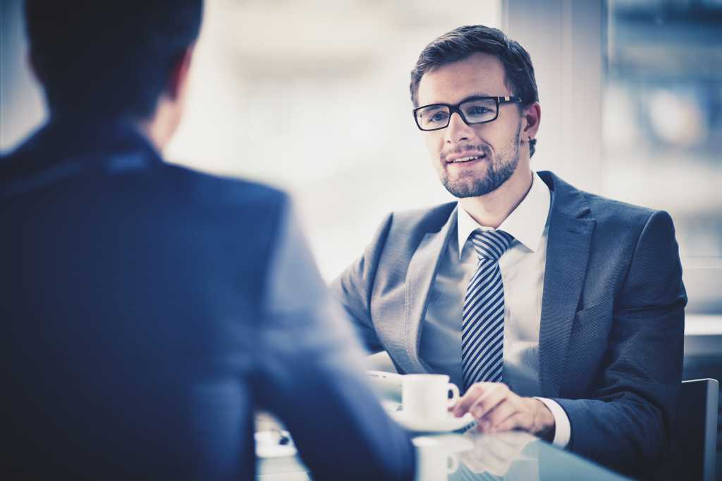 Image of young businessman with cup of coffee communicating with his colleague