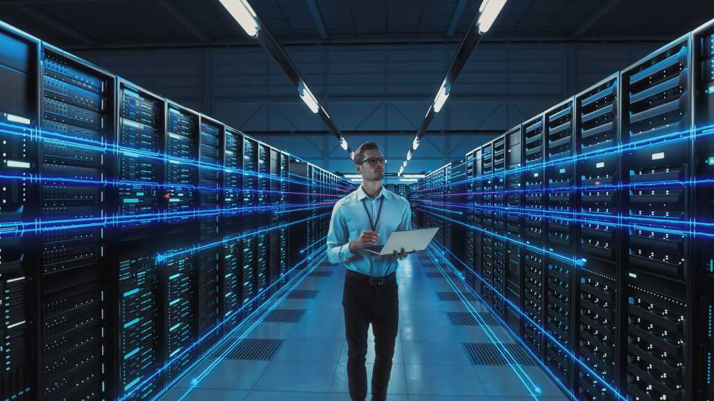 Futuristic Concept: Data Center Chief Technology Officer Holding Laptop, Standing In Warehouse, Information Digitalization Lines Streaming Through Servers. SAAS, Cloud Computing, Web Service