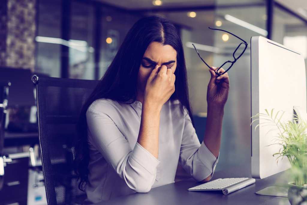 A stressed businesswoman with a headache rubs her eyes, pinching her brow.
