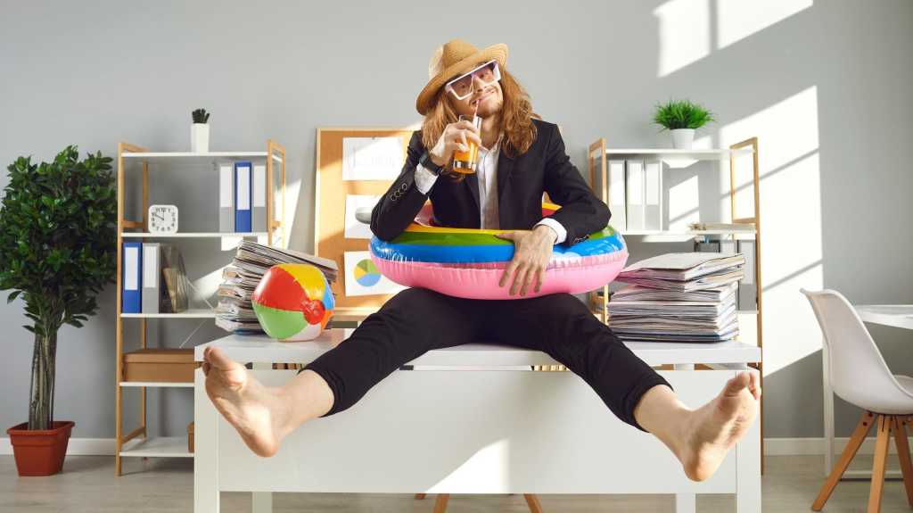 Annual leave and planning travel vacation concept. Funny office worker waiting for summer holidays. Happy barefoot employee in sun hat, sunglasses and swim ring sitting on desk and drinking cocktail