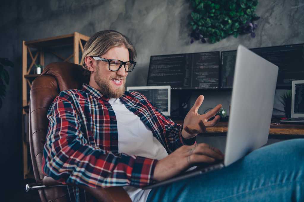 Photo of young blond bearded guy it support specialist wear plaid shirt sitting armchair confused looking at bug website indoors office