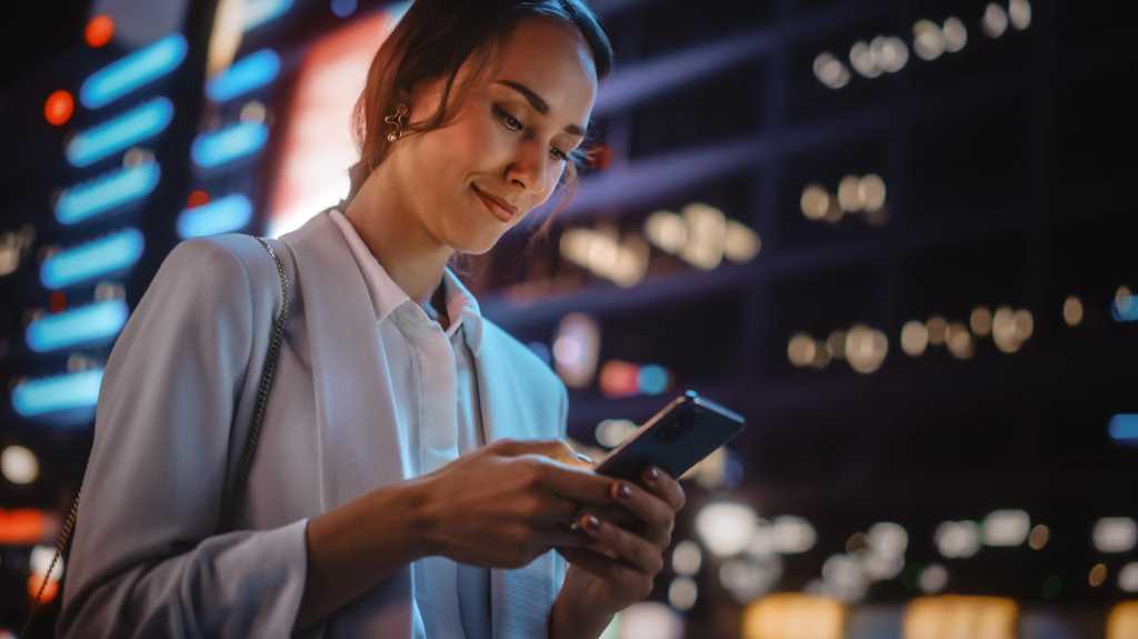 Schöne junge Frauen mit Smartphone, die in der nächtlichen Stadtstraße mit Neon Light spazieren gehen. Portrait von wunderschönen Lächeln Frauen mit dem Handy. Nieder-Tilt-Up-Aufnahme
