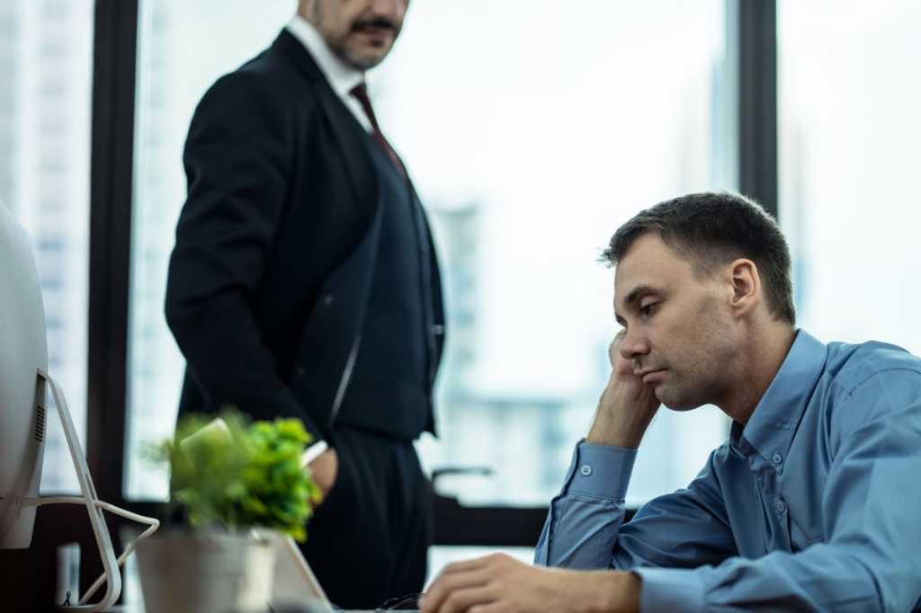 Man working under pressure by their boss standing behind and forcing them to complete job