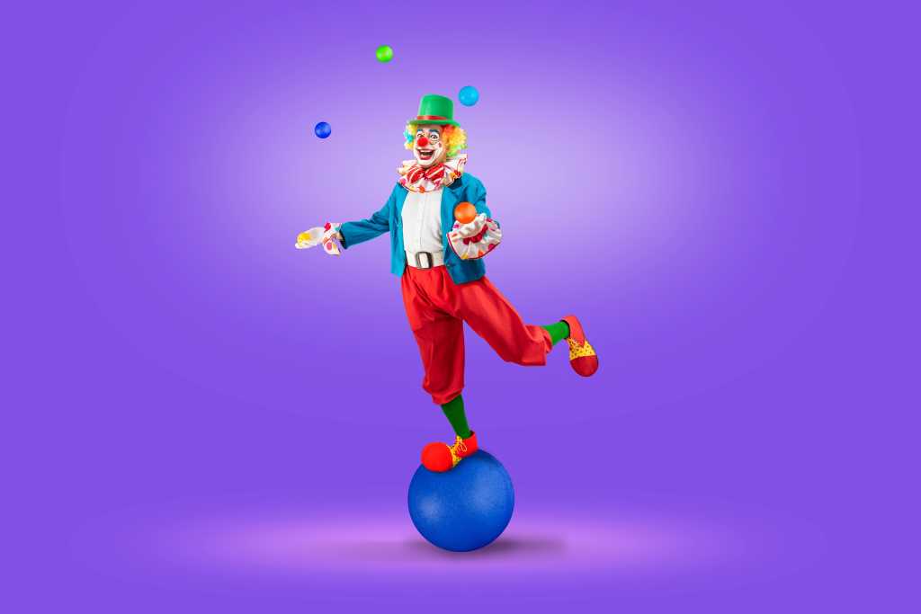 Funny juggler clown juggling balls in the circus, man entertainer as Joker in a suit and wig, with clown whiteface makeup. Trickster, jester, pantomime, mime, and a professional actor at events
