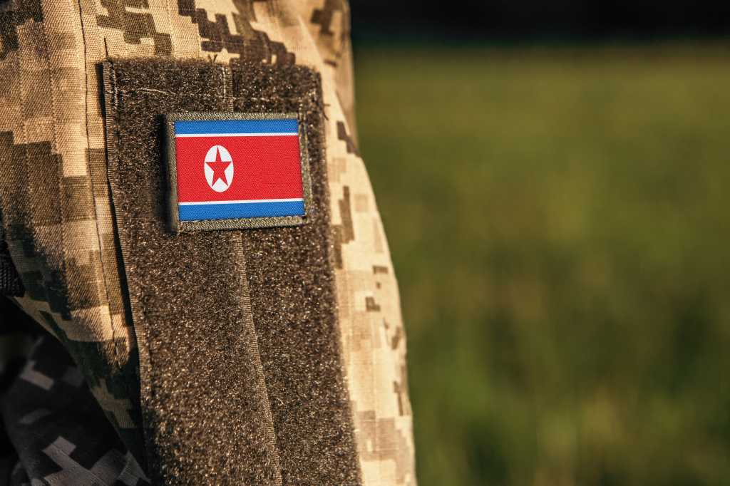 Close up millitary woman or man shoulder arm sleeve with North Korea flag patch. Troops army, soldier camouflage uniform. Armed Forces, empty copy space for text