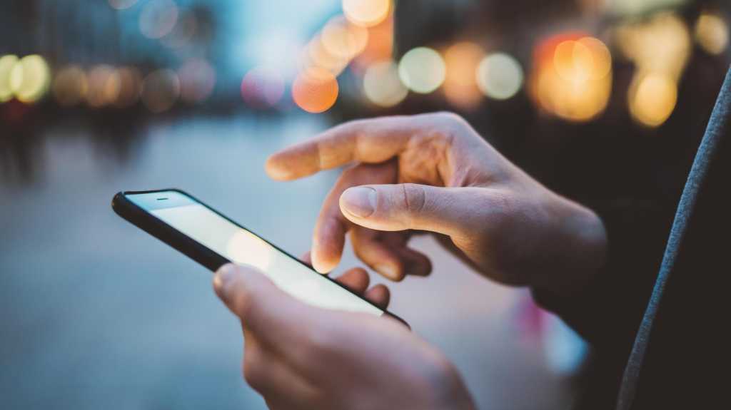 Close-up image of male hands using smartphone at night on city shopping street, searching or social networks concept, hipster man typing an sms message to his friends