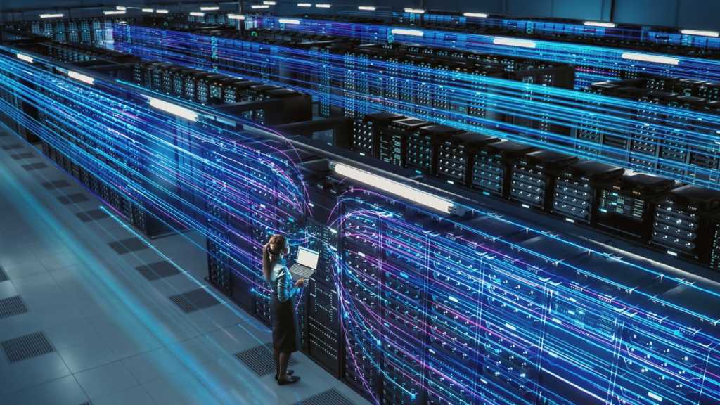 Image of big data center with female officer standing and holding a laptop