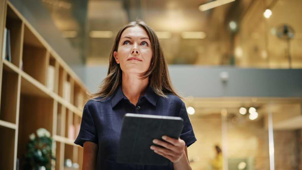 Close Up of a Content Female CEO Making Notes on her Tablet. Portrait of a Caucasian Woman Crossing a Corporate Office Hall, Smiling and Looking Confident. Low Angle