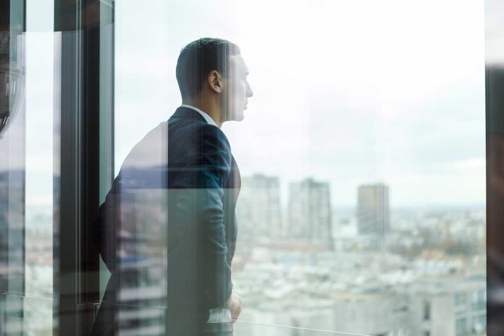 Business man looking out through the office balcony seen through glass doors.