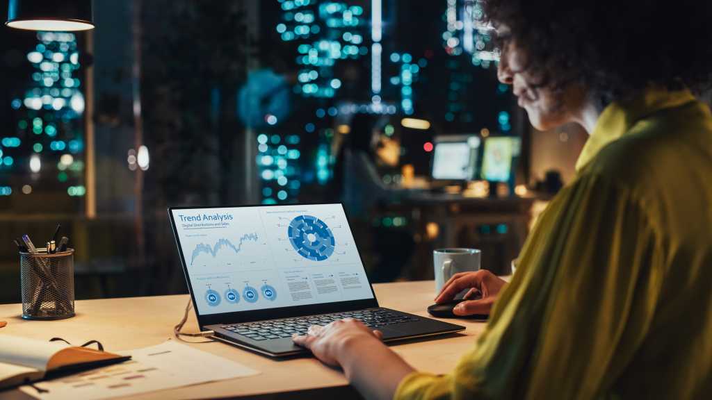 Creative Multiethnic Female Working on Laptop Computer with a Sales Statistics and Chart Displayed on Screen. Successful Designer Developing a Marketing Strategy, Preparing a Presentation