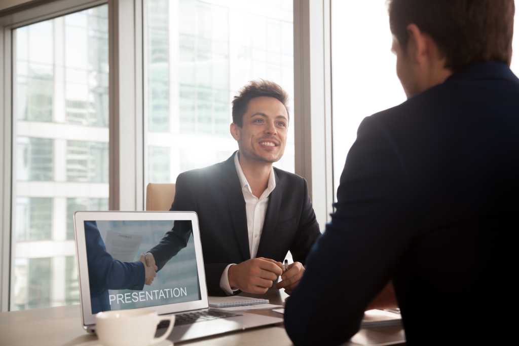 Smiling investment broker showing digital presentation on laptop screen to client, friendly salesman giving sales pitch, making business proposal to partner, selling product, offering cooperation
