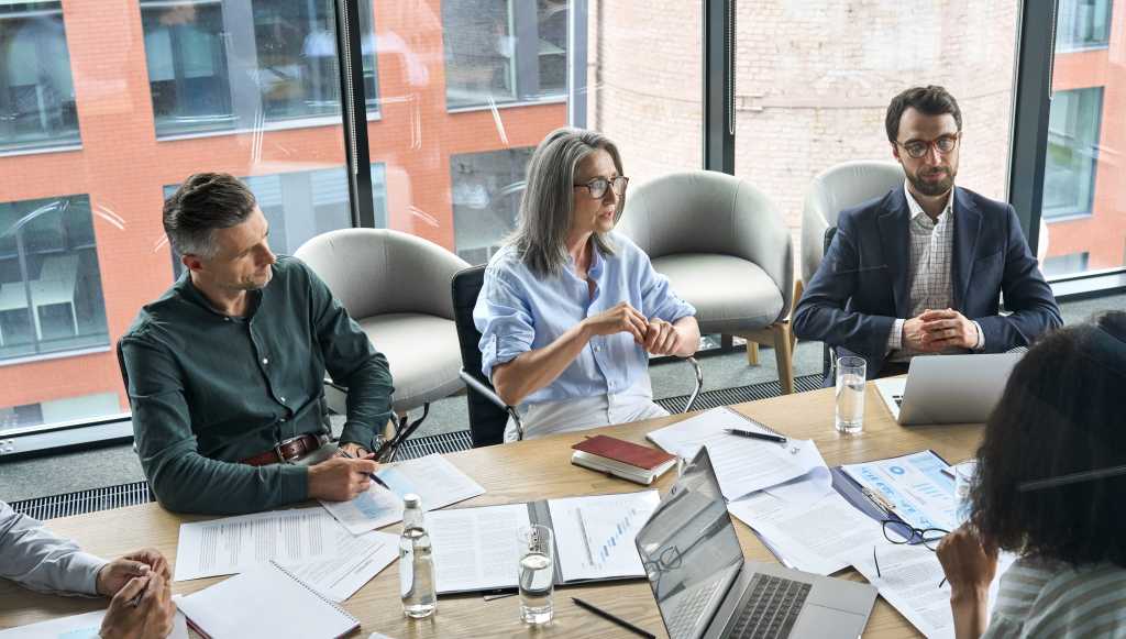Professional executive businesspeople discuss corporation project planning sit at meeting table in boardroom. Company managers brainstorm financial plan working together with document papers in office