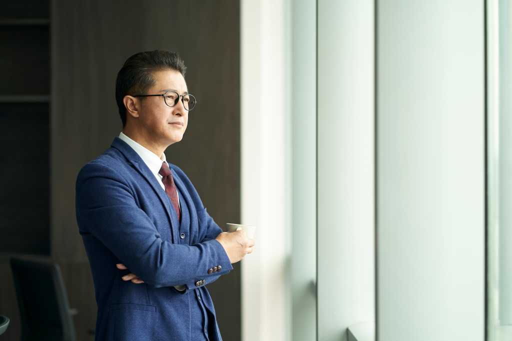 portrait of a asian business leader senior manager standing by window thinking