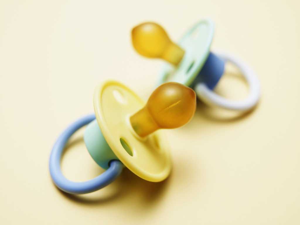 Two baby pacifiers on yellow background
